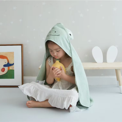 Un enfant assis portant sa cape de bain bebe de couleur verte avec sa capuche en forme de grenouille.