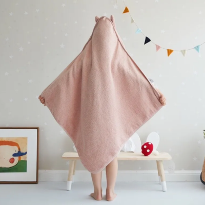 Un enfant de dos portant la cape de bain bebe avec un design de lapin, de couleur rose pâle.