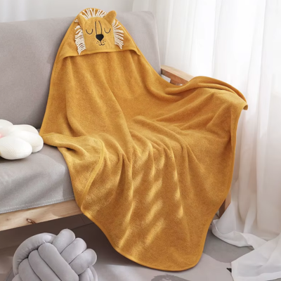 Sur un fauteuil gris est posé une cape de bain bebe de couleur orange. Sa capuche à la forme de tête de lion ornée d'une crinière à franche dans une pièce lumineuse.