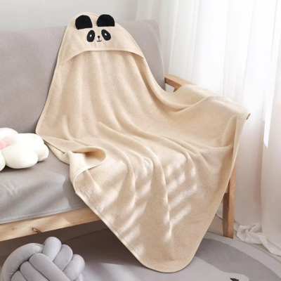 Une cape de bain bebe blanche, soigneusement disposée sur un canapé. La capuche, ornée d’un visage de panda avec des oreilles noires, met en valeur le design adorable et la praticité du produit.